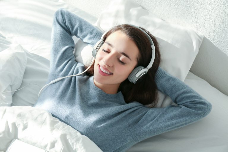 a beautiful girl is sleeping on the bed with headphone on