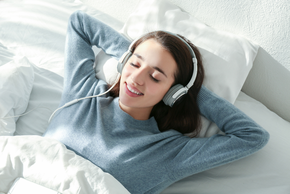 a beautiful girl is sleeping on the bed with headphone on