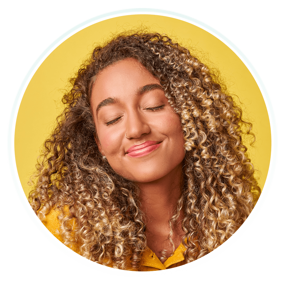 A young woman with curly hair with closed eyes and a big smile.