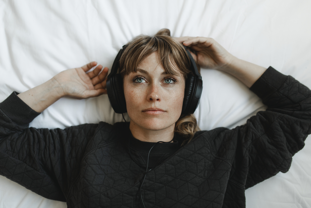 This image shows an isolated woman lying on bed with a headphone on
