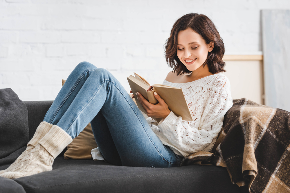 This image shows a girl sitting on the sofa and reading an inspirational book